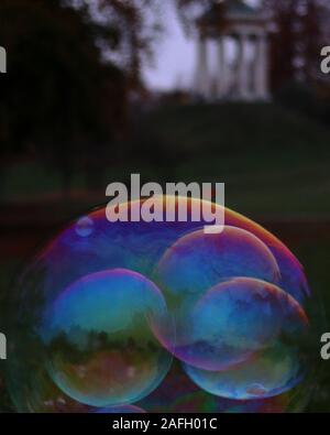 Closeup of soap bubbles in a garden with greenery and a building on a blurry background Stock Photo