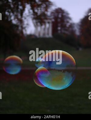 Closeup of soap bubbles in a garden with greenery and a building on a blurry background Stock Photo