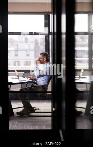 Middle aged white businessman drinking coffee and working alone in a meeting room, vertical Stock Photo