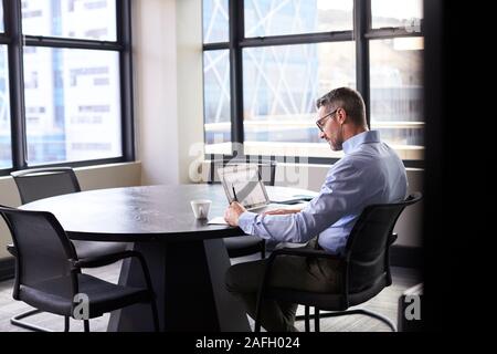 Middle aged white businessman working alone in a meeting room, seen from doorway Stock Photo