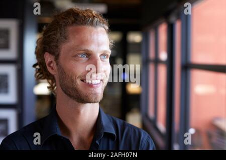 Millennial white male business creative smiling and looking out of the window in an office, close up Stock Photo