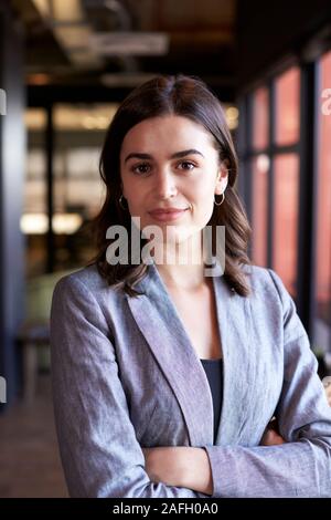 Millennial white businesswoman standing with arms crossed smiling to camera in an office, close up Stock Photo