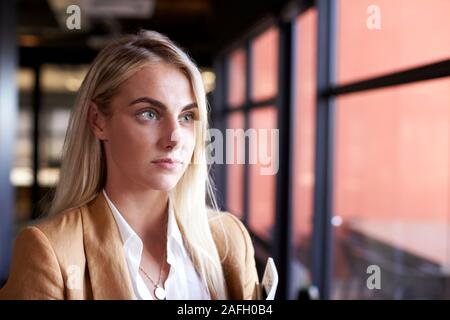 Millennial white blonde businesswoman looking out of the window in an office, head and shoulders Stock Photo