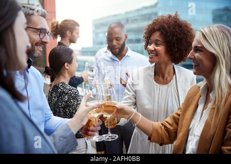 Socialising office colleagues raising glasses and making a toast with drinks after work Stock Photo