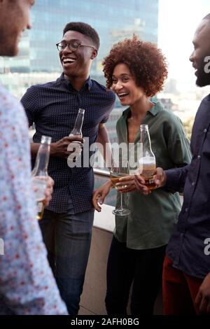 Smiling creative business colleagues socialising with drinks after work, vertical Stock Photo