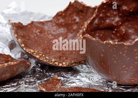 Broken chocolate Easter egg with chopped hazelnuts on a foil sheet against, UK. Stock Photo
