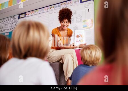 Female Teacher Reading Story To Group Of Elementary Pupils In School Classroom Stock Photo