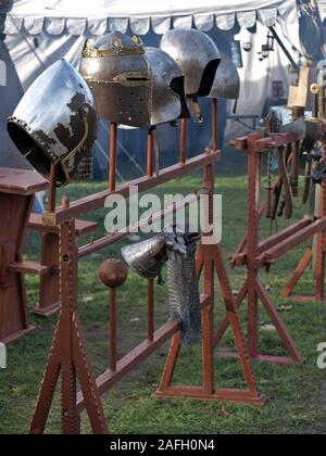 Knight helmets and weapons on display on a wooden stand at a medieval market in Mülheim Ruhr. Smoke is in the air.Tents in the blurred background Stock Photo