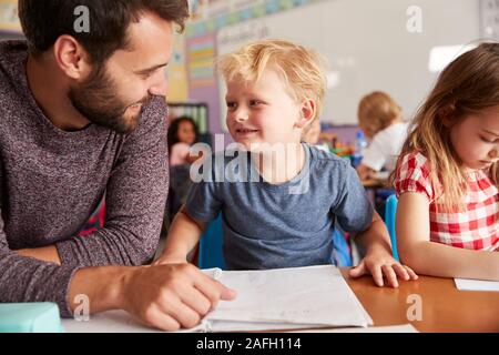 Elementary School Teacher Giving Male Pupil One To One Support In Classroom Stock Photo