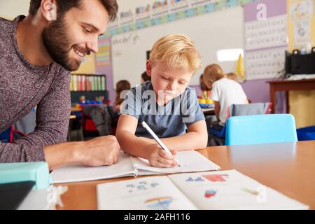 Elementary School Teacher Giving Male Pupil One To One Support In Classroom Stock Photo
