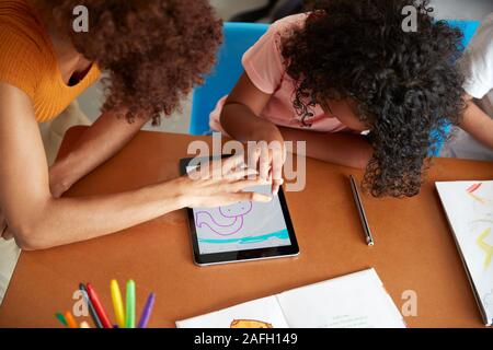 Elementary School Teacher And Female Pupil Drawing Using Digital Tablet In Classroom Stock Photo