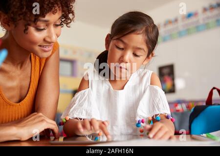 Elementary School Teacher And Female Pupil Drawing Using Digital Tablet In Classroom Stock Photo