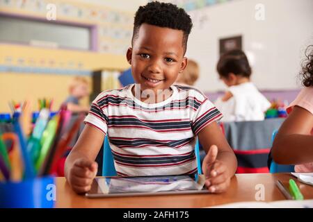 Portrait Of Male Pupil In Elementary School Drawing Using Digital Tablet In Classroom Stock Photo
