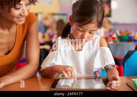 Elementary School Teacher And Female Pupil Drawing Using Digital Tablet In Classroom Stock Photo