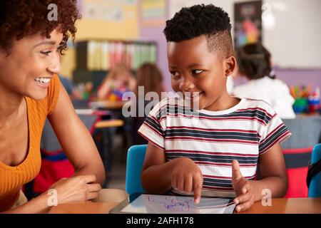 Elementary School Teacher And Male Pupil Drawing Using Digital Tablet In Classroom Stock Photo