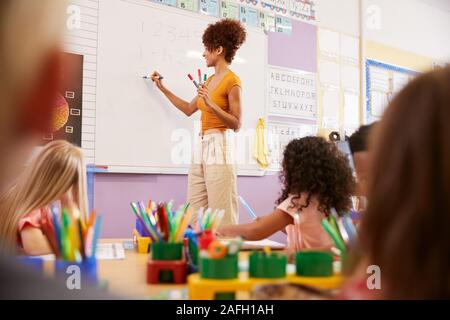 Female Teacher Standing At Whiteboard Teaching Maths Lesson To Elementary Pupils In School Classroom Stock Photo