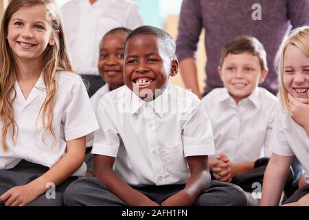 Group Of Elementary School Pupils Wearing Uniform Sitting On Floor Listening To Teacher Stock Photo