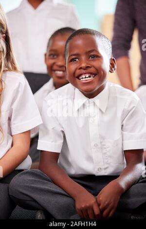 Group Of Elementary School Pupils Wearing Uniform Sitting On Floor Listening To Teacher Stock Photo