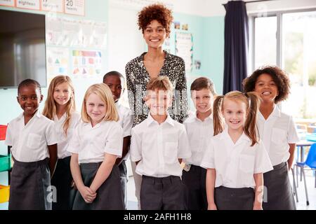 Portrait Of Elementary School Pupils Wearing Uniform Standing In Classroom With Female Teacher Stock Photo
