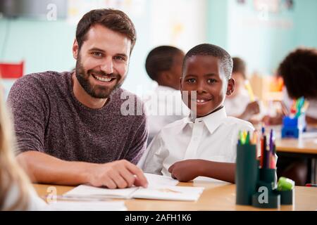 Portrait Of Elementary School Teacher Giving Male Pupil Wearing Uniform One To One Support In Class Stock Photo
