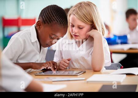 Two Elementary School Pupils Wearing Uniform Using Digital Tablet At Desk Stock Photo