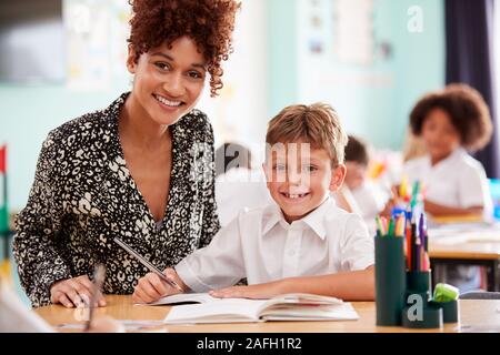 Portrait Of Woman Elementary School Teacher Giving Male Pupil Wearing Uniform One To One Support Stock Photo
