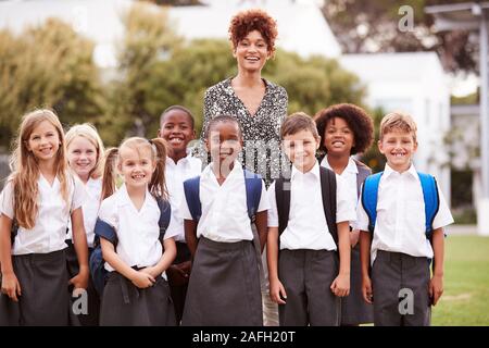 Outdoor Portrait Of Elementary School Pupils With Teacher Wearing Uniform Standing On Playing Field Stock Photo