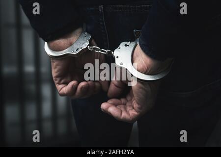 arrested man with cuffed hands behind prison bars Stock Photo