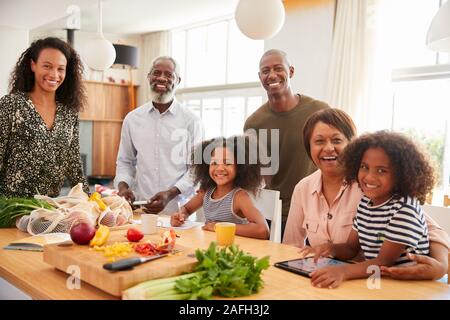 Portrait Of Grandparents Sitting At Table With Grandchildren Playing Games As Family Prepares Meal Stock Photo