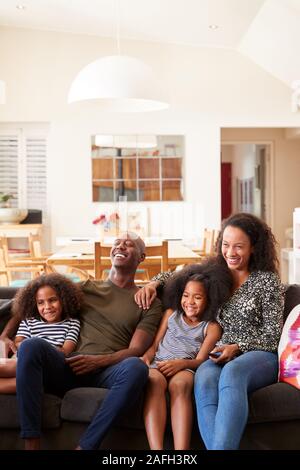 Family Sitting On Sofa At Home And Watching Movie On TV Together Stock Photo