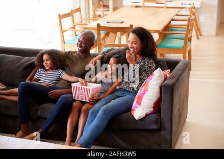Family Sitting On Sofa At Home Eating Popcorn And Watching Movie Together Stock Photo
