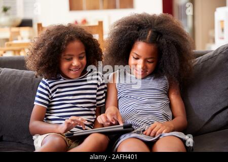 Brother And Sister Sitting On Sofa At Home Playing With Digital Tablet Stock Photo