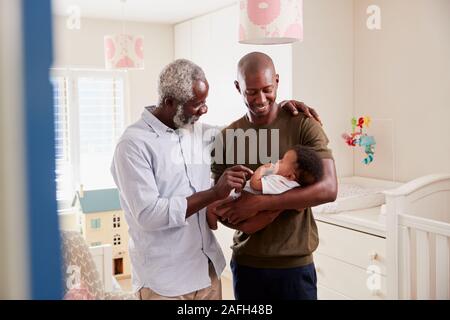 Proud Grandfather With Adult Son Cuddling Baby Grandson In Nursery At Home Stock Photo