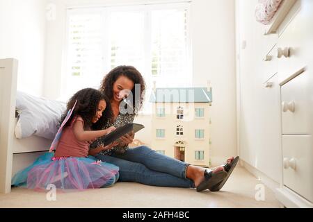 Mother With Daughter Sitting On Bed In Childs Bedroom Using Digital Tablet Together Stock Photo
