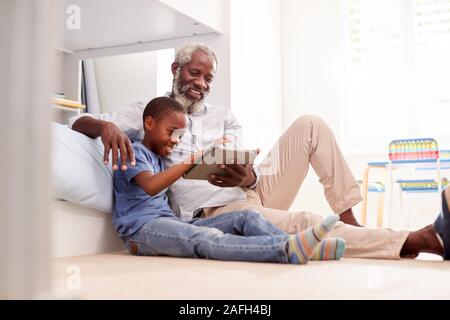 Grandfather Sitting With Grandson In Childs Bedroom Using Digital Tablet Together Stock Photo