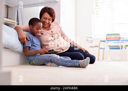 Grandmother Sitting With Grandson In Childs Bedroom Using Digital Tablet Together Stock Photo