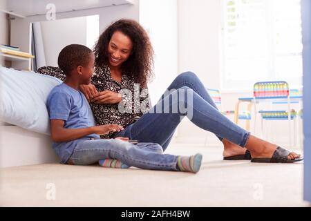 Mother With Son Sitting On Bed In Childs Bedroom Using Digital Tablet Together Stock Photo