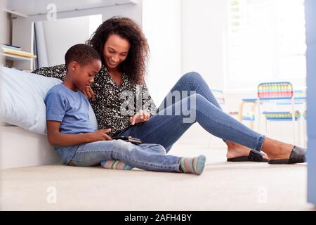 Mother With Son Sitting On Bed In Childs Bedroom Using Digital Tablet Together Stock Photo
