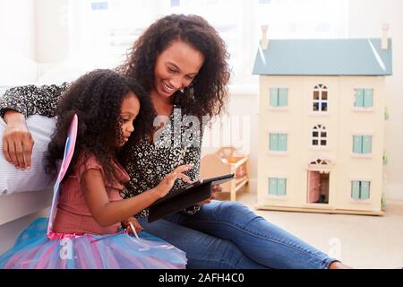 Mother With Daughter Sitting On Bed In Childs Bedroom Using Digital Tablet Together Stock Photo