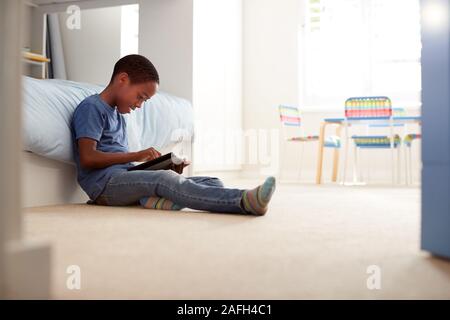 Boy Sitting On Floor In Bedroom Using Digital Tablet Stock Photo