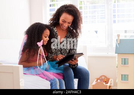 Mother With Daughter Sitting On Bed In Childs Bedroom Using Digital Tablet Together Stock Photo