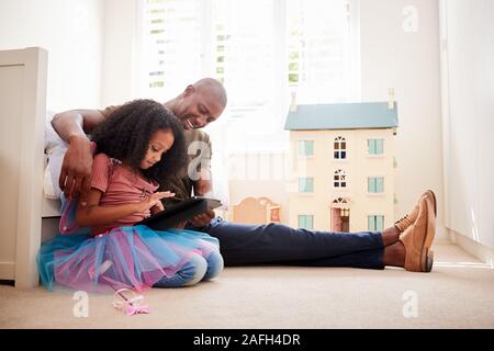 Father With Daughter Sitting On Bed In Childs Bedroom Using Digital Tablet Together Stock Photo