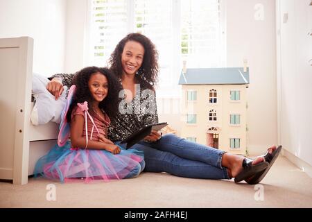 Portrait Of Mother With Daughter Sitting On Bed In Childs Bedroom Using Digital Tablet Together
