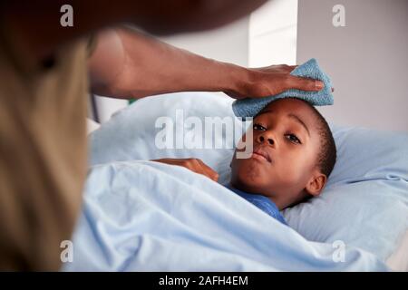 Father Caring For Sick Son Ill In Bed With Temperature