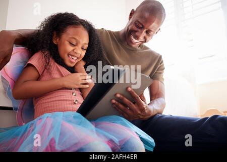Father With Daughter Sitting On Bed In Childs Bedroom Using Digital Tablet Together Stock Photo