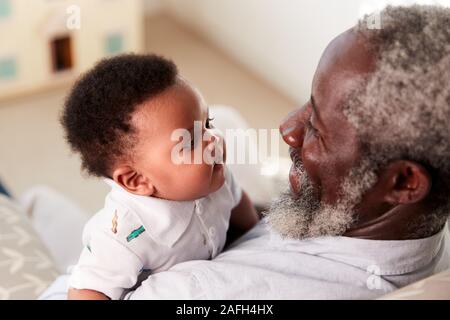 Proud Grandfather Cuddling Baby Grandson In Nursery At Home Stock Photo