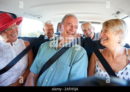 Group Of Senior Friends Sitting In Back Of Van Being Driven To Vacation Stock Photo