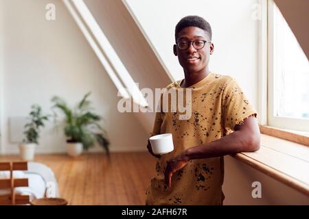 Portrait Of Young Man Relaxing In Loft Apartment With Hot Drink Stock Photo