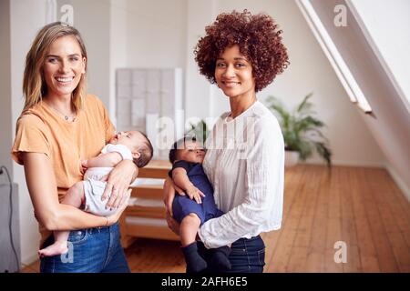 Portrait Of Two Mothers Meeting Holding Newborn Babies At Home In Loft Apartment Stock Photo