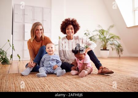 Portrait Of Two Mothers Meeting For Play Date With Babies At Home In Loft Apartment Stock Photo